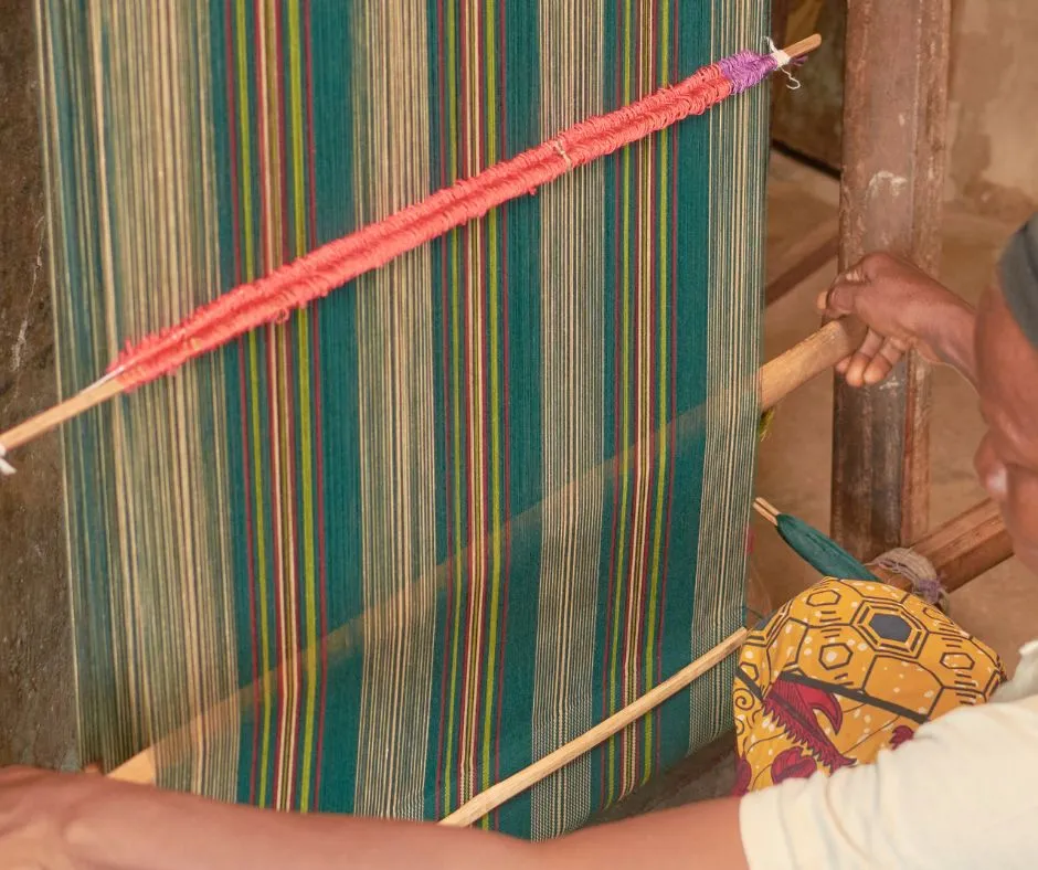 An African female aso oke weaver using a single heddle loom. (Circa 2020)