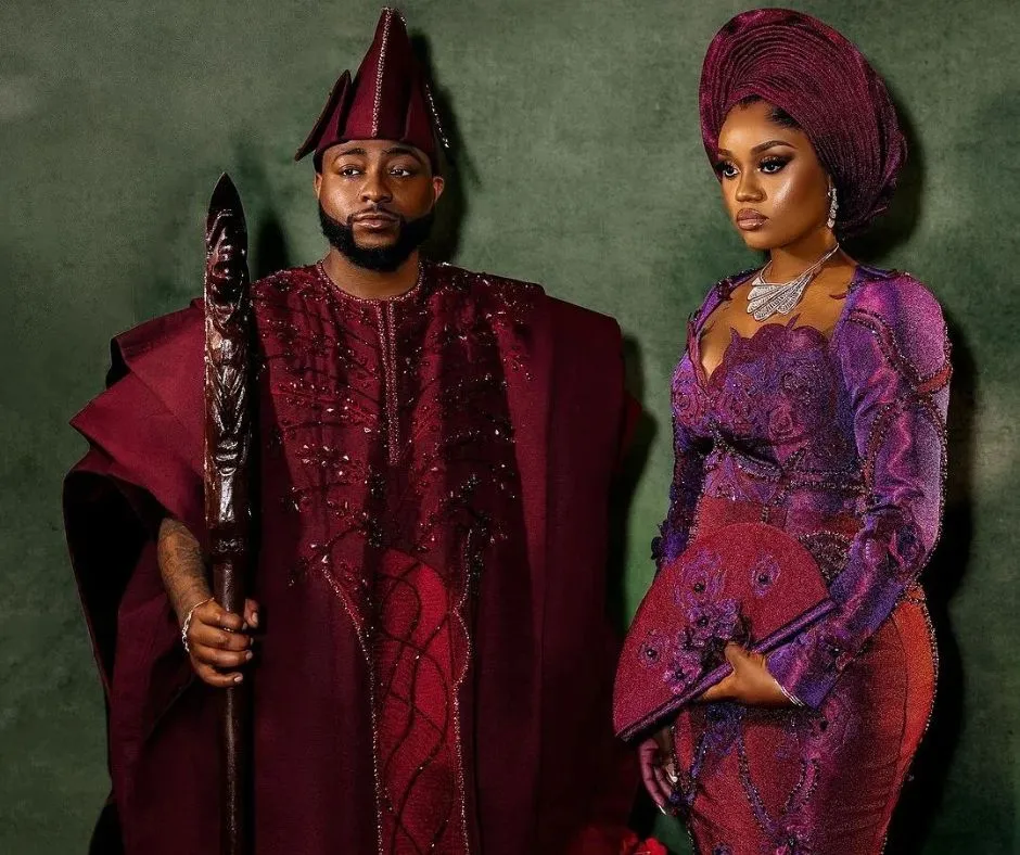 Davido and Chioma in their high profile wedding aso oke, davido is wearing a burgundy colored agbada while chioma is wearing a duotone aso oke dress and gele with cutout detailing.