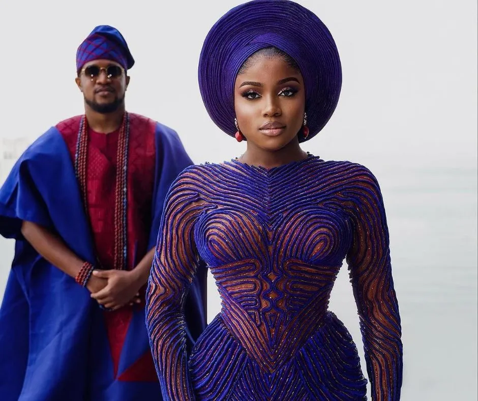 Veekee James and her husband in matching wedding aso oke. Veekee is in a blue and red duotuoned aso oke dress while her husband is wearing a blue aso oke agbada