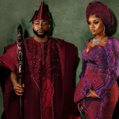 Davido and Chioma in their high profile wedding aso oke, davido is wearing a burgundy colored agbada while chioma is wearing a duotone aso oke dress and gele with cutout detailing.